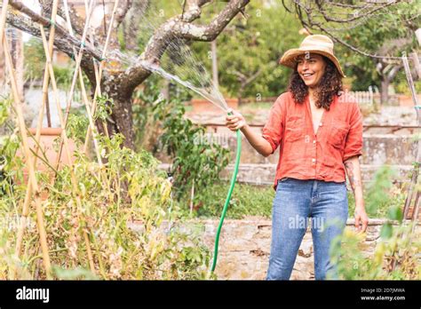 Smiling Beautiful Mature Woman Watering Plants From Hose At Garden Stock Photo Alamy