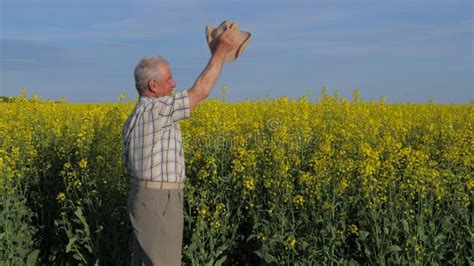 Elderly And White Haired Farmer In A Field Waving His Arms And Hat In