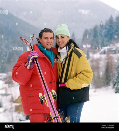 1990’s Winter retro SKI fashion style couple in colourful skiing outfits pose together in snowy ...