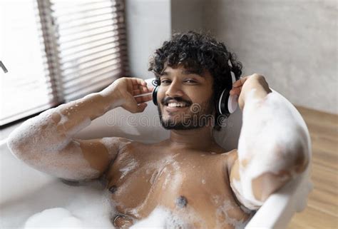 Calm Indian Man In Wireless Headphones Lying In Hot Bubbly Bath And Enjoying His Playlist In