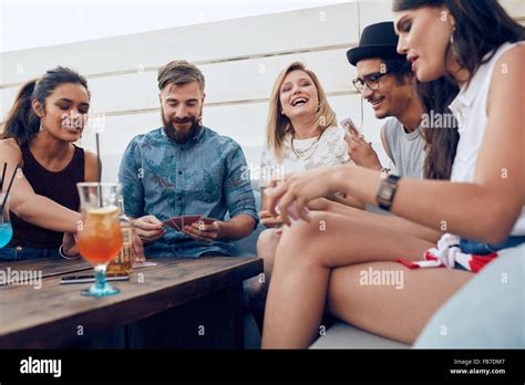 Group Of Friends Sitting At A Wooden Table And Playing Cards Cheerful