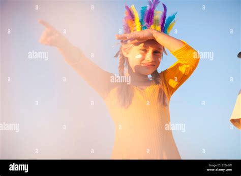 Girl dressed as native american in feather headdress with hand shading eyes and pointing Stock ...