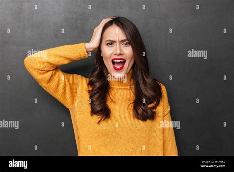 Angry Brunette Woman In Sweater Holding Her Head And Looking At The Camera Over Black Background