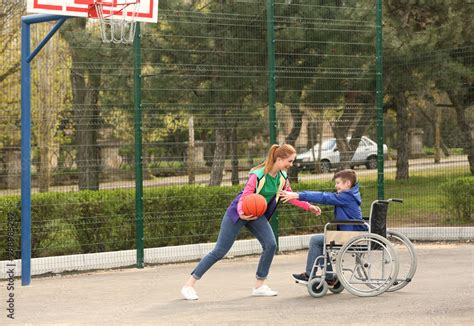 Preteen boy in wheelchair and young woman playing basketball on sports ...