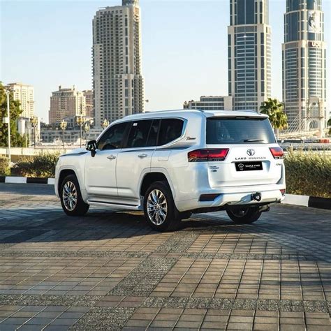 The Rear End Of A White Toyota Land Cruiser Parked In Front Of A Cityscape