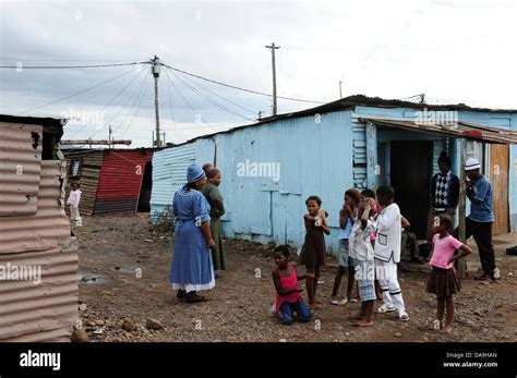 Group Of Children Standing In Front Of Shacks Talking To Adults At