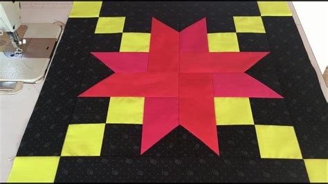 A Black And Yellow Quilt With A Red Star On It S Center Next To A