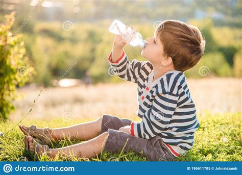 A Beautiful Child Sitting On The Grass Drinks Water From A Bottle In