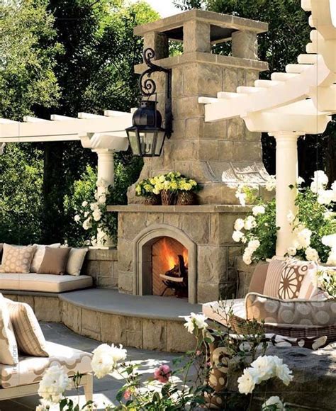 An Outdoor Fireplace With Lots Of Seating Around It And Flowers On The