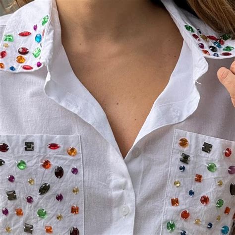 A Close Up Of A Person Wearing A White Shirt With Multi Colored Stones