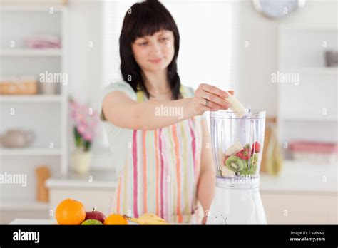 Pretty Brunette Woman Putting Vegetables In A Mixer While Standing