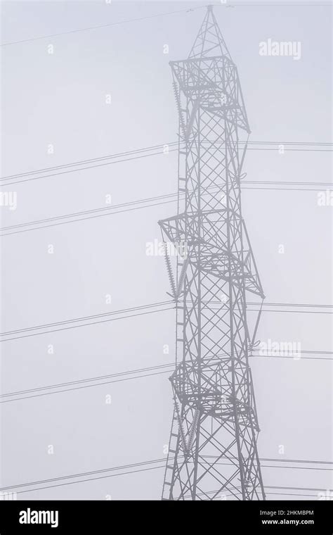 A Large High Voltage Pylon Is Shrouded In The Morning Mist Stock Photo