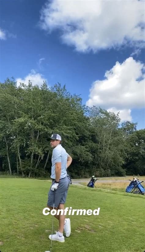 A Man Standing On Top Of A Lush Green Field Next To A Golf Ball And Tee