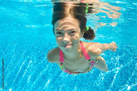 Child swims in pool underwater, happy active girl dives and has fun in water, kid fitness and ...