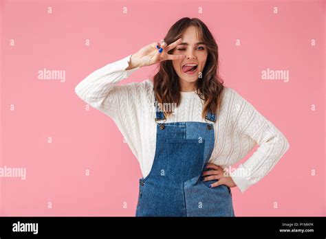 Cheerful Brunette Woman In Casual Clothes Posing With Arm On Hip While Showing Peace Gesture And