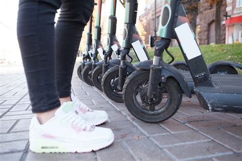 Mujer irreconocible de pie delante de scooters eléctricos alineados en