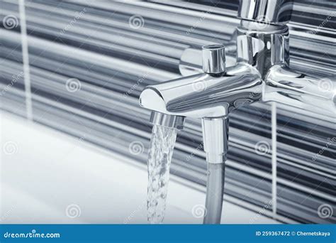 Water Flowing From Bath Tap Installed On Black And White Wall Stock