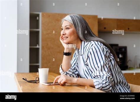 Happy White Haired Mature Woman Drinking Coffee And Using Mobile Phone