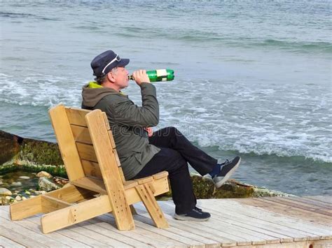 Un Hombre Bebiendo Cerveza Sentado En Una Tumbona De Madera Junto Al