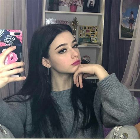 A Woman Taking A Selfie In Front Of A Book Shelf With Her Phone Up To