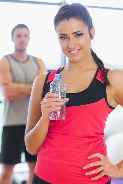 Fit Mujer Sosteniendo La Botella De Agua Con Un Amigo En Segundo Plano