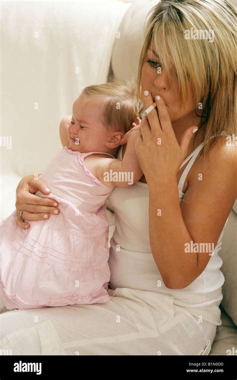 Young mother smoking with her crying nine month old baby sitting on her ...