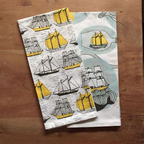 Two Napkins With Yellow Sailboats On Them Sitting On A Wooden Table