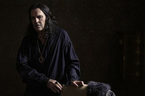 a man with long black hair standing next to a stuffed animal in a dark room