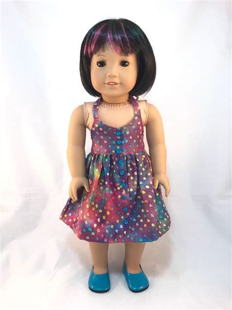 A Doll With Black Hair Wearing A Purple Dress And Blue Shoes Is