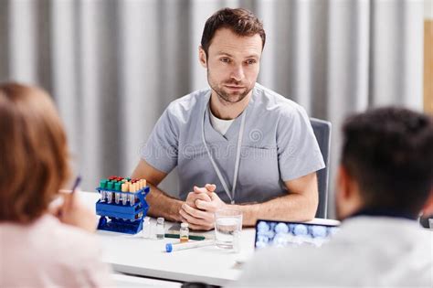 Young Confident Lab Worker In Medical Scrubs Looking At Colleague Stock