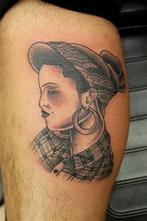 A Woman With A Hat And Hoop Earrings On Her Thigh Is Shown In This Tattoo