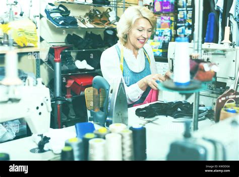 Glad Mature Woman Tailor Using Sewing Machine At Atelier Stock Photo