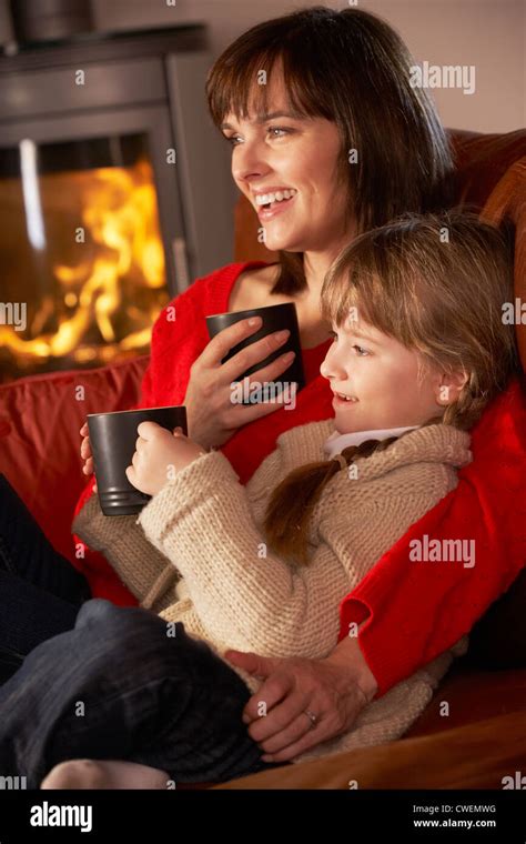 Mother And Daughter Relaxing With Hot Drink Watching TV By Cosy Log Fire Stock Photo Alamy