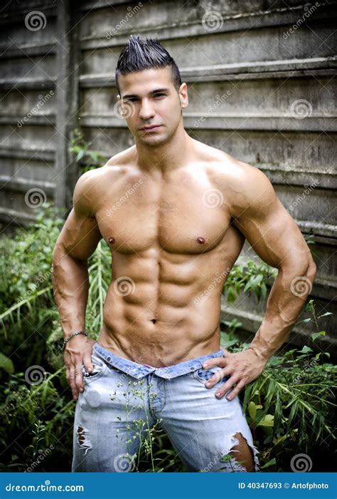 Muscular Young Latino Man Shirtless In Jeans In Front Of Concrete Wall