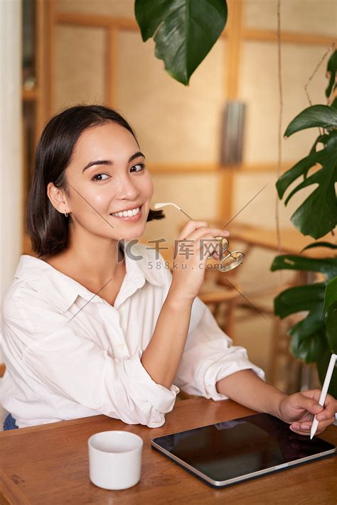 美丽的亚洲女孩坐在咖啡馆里喝杯咖啡，用图形笔在数字平板电脑上画画，轻而易举地画画高清摄影大图 千库网