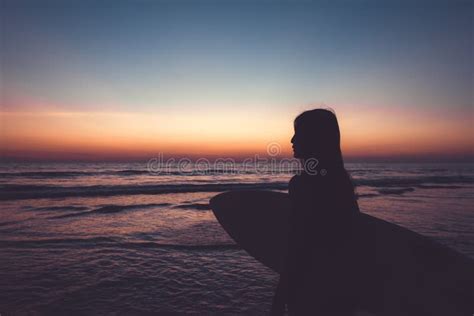 Silhouette Of Beautiful Surfer Female With Surfboard On The Sandy Beach