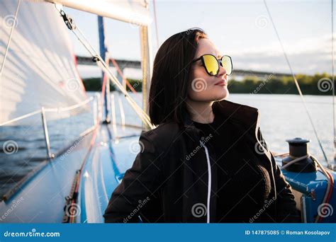 Young Smiling Dark Haired Woman Wearing Sunglasses Sitting On A Board