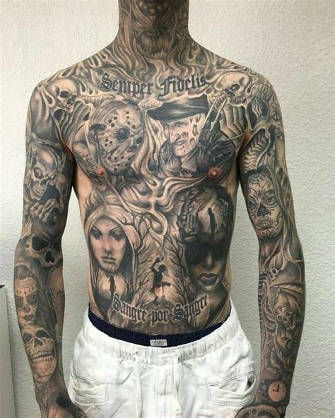 A Man With Many Tattoos On His Body And Chest Is Standing In Front Of A White Wall