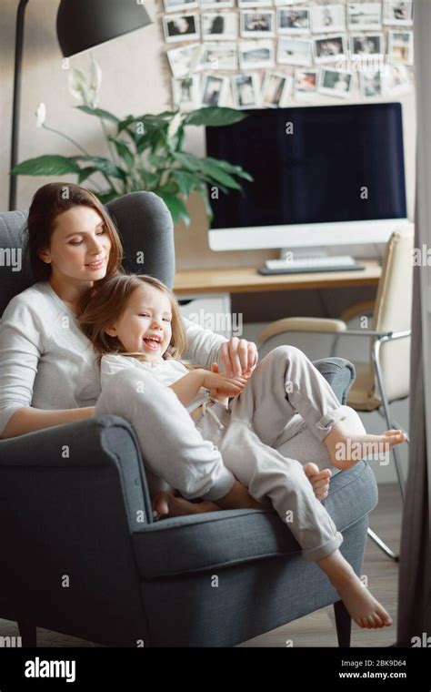 Mother With A 3 Year Old Daughter Sit In A Gray Armchair Hug And Laugh