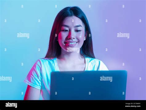 Work or play at computer. Smiling asian girl looking at laptop in neon Stock Photo - Alamy