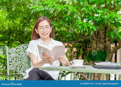 Asian Middle Aged Woman In Glasses Reading A Book In Backyard Stock