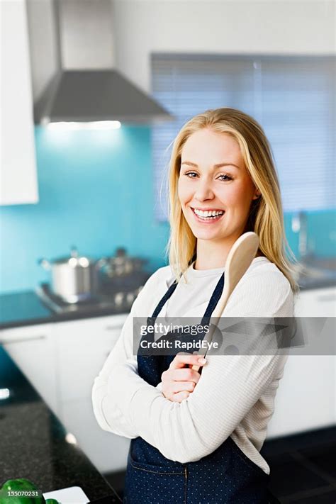 Happy Blonde Home Maker With Wooden Spoon In Modern Kitchen High Res