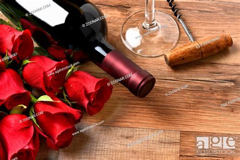 A Wine Bottle With Red Roses And A Glass And Cork Screw On A Rustic