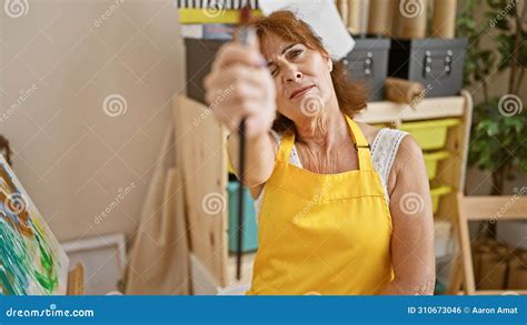 A Mature Woman In A Yellow Apron Focuses Intently While Painting On A