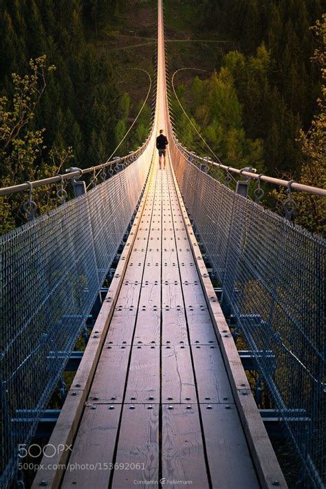 A Person Walking Across A Suspension Bridge In The Middle Of Trees And