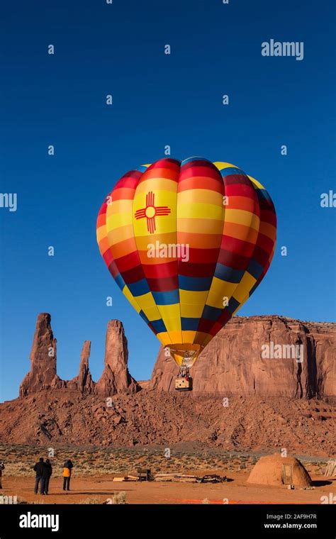 A Hot Air Balloon Flies Over A Traditional Hogan In Front Of The Three