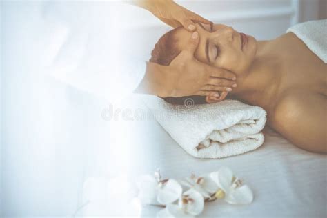 Beautiful Brunette Woman Enjoying Facial Massage With Closed Eyes In Sunny Spa Center Relaxing