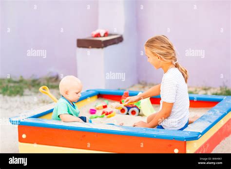 Cute Baby Boy Playing With His Sister With Toys In The Sandbox Outdoor