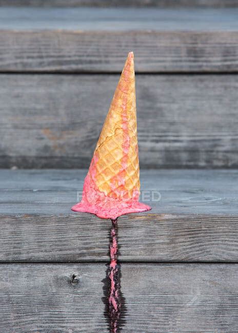 From Above Of Pink Ice Cream In Wafer Cone Dropped On Wooden Plank