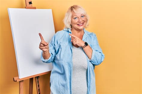 Premium Photo Middle Age Blonde Woman Standing By Painter Easel Stand